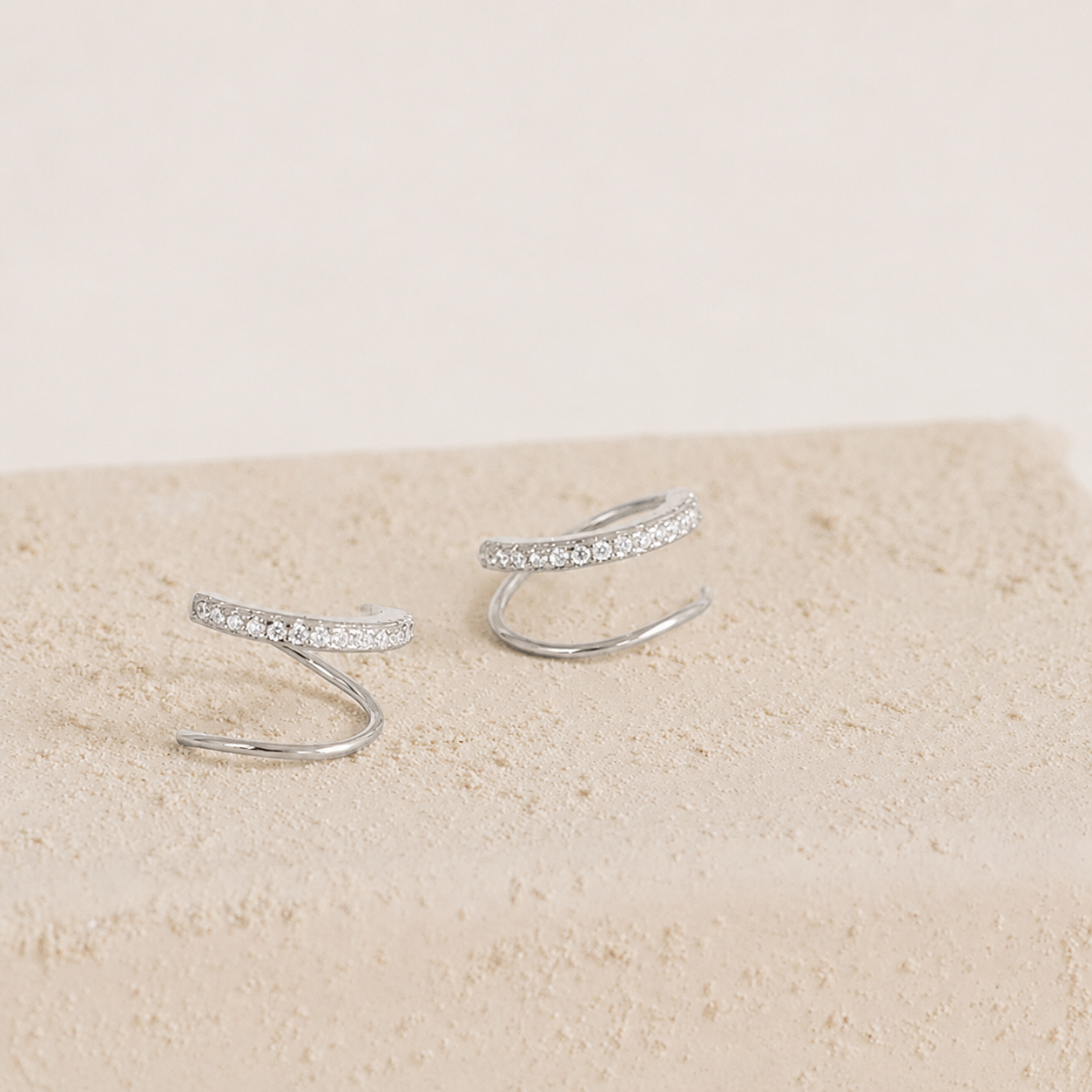 Silver ear cuffs with small stones on a beige surface